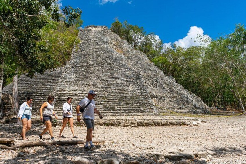 A large ancient pyramid with tourists walking around it. 5