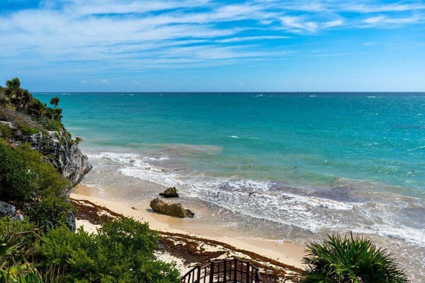 A coastal landscape with a sandy beach, rocky outcrops, and a clear blue sky. 1