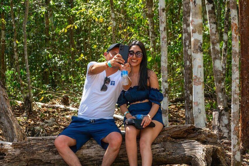 Two people sitting on a log in a forest with trees in the background. 3