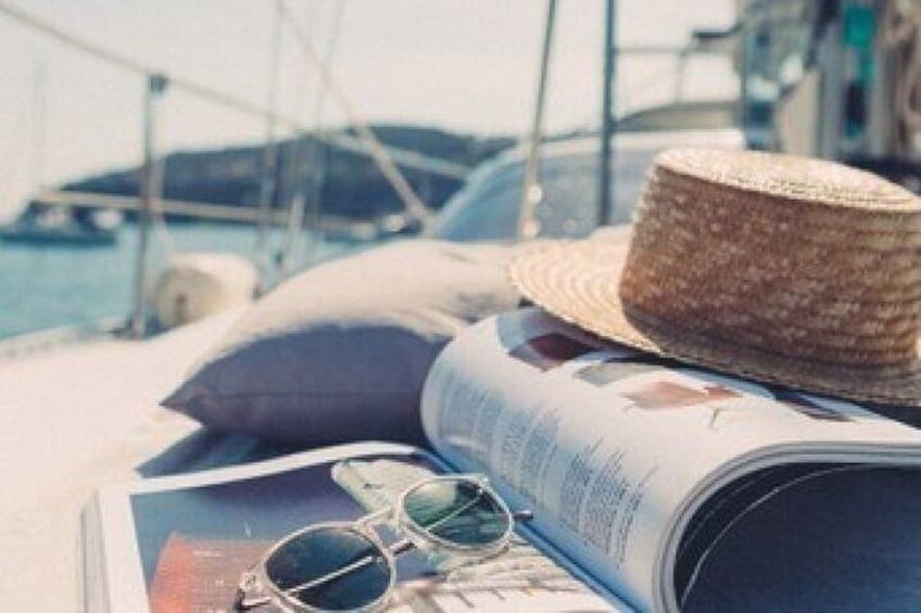 A straw hat, sunglasses, and a magazine on a boat with a marina in the background. 4