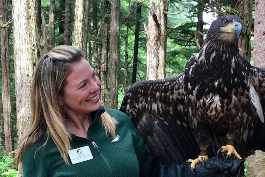 Una persona con una chaqueta verde y una identificación de nombre parada junto a una rapaz en un bosque. 3
