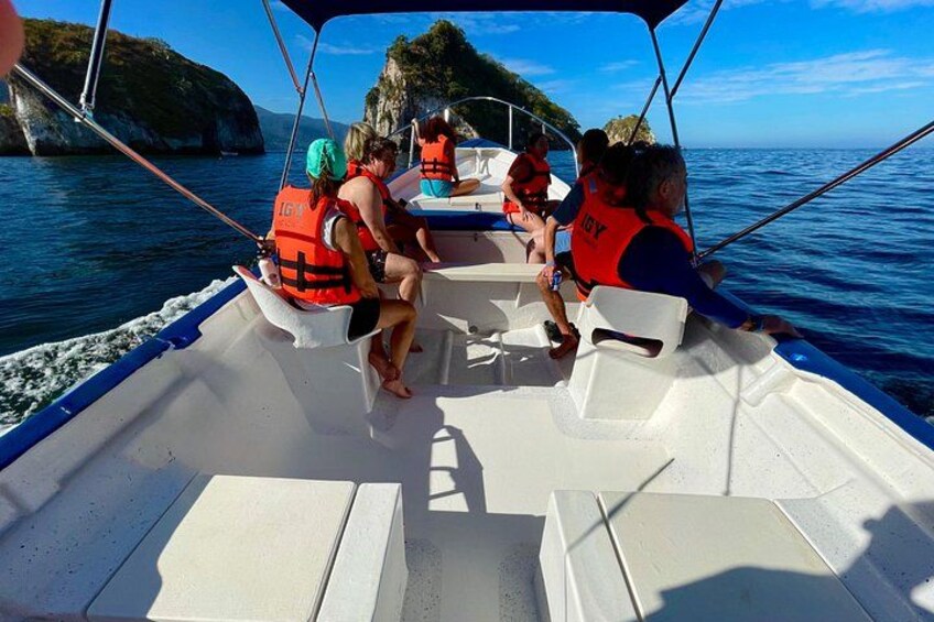 A boat with people wearing life jackets, surrounded by calm water and rocky cliffs. 2