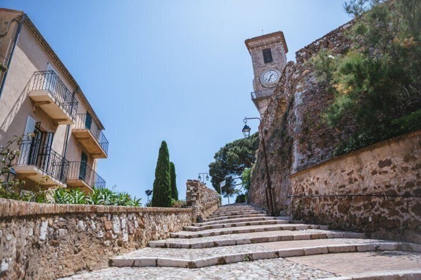 A stone staircase leading up to a tower with a clock, surrounded by buildings and greenery. 5