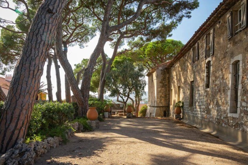 A stone building with arched windows, surrounded by trees and a dirt path. 4