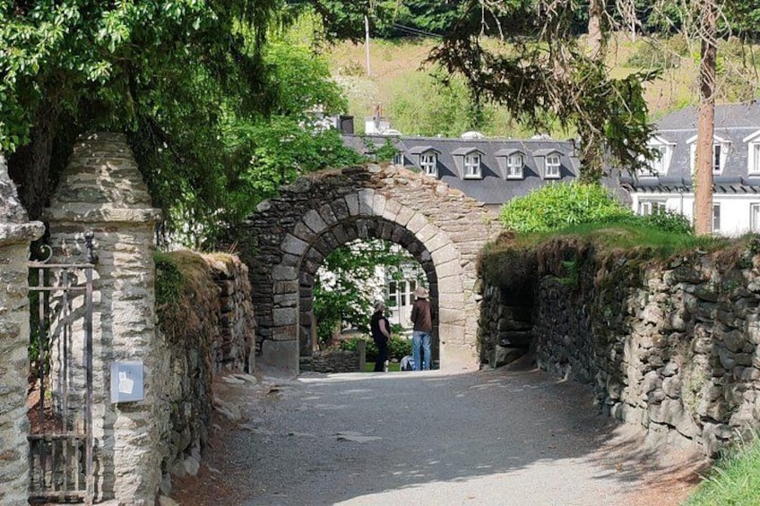 Ein steinerer Bogen führt zu einer Straße, umgeben von Steinmauern und viel Grün. 5