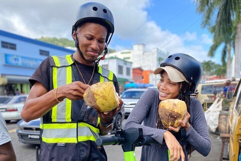 Two people wearing helmets and safety vests, holding coconuts. 1