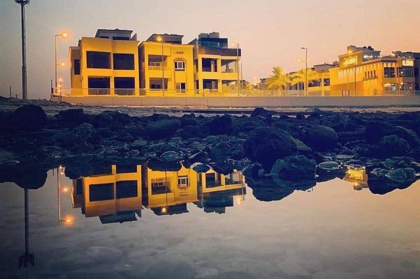 A waterfront with buildings reflecting on calm water, surrounded by rocks. 5