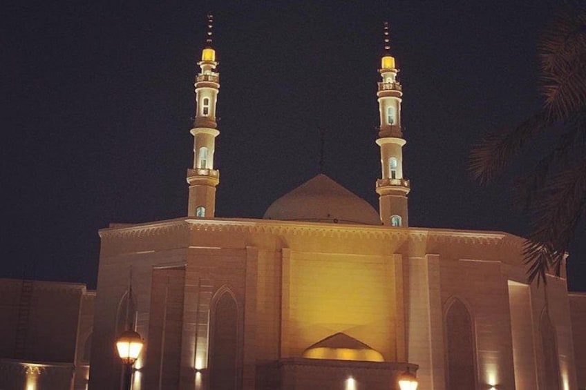 A mosque with two minarets and a dome, illuminated at night. 2