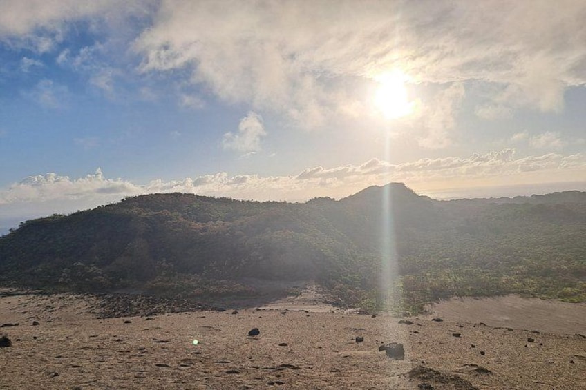 Ein Strand mit einem Berg im Hintergrund und der Sonne, die durch die Wolken scheint. 1