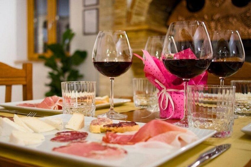 A table with plates of cured meats, glasses of red wine, and a pink gift basket. 1