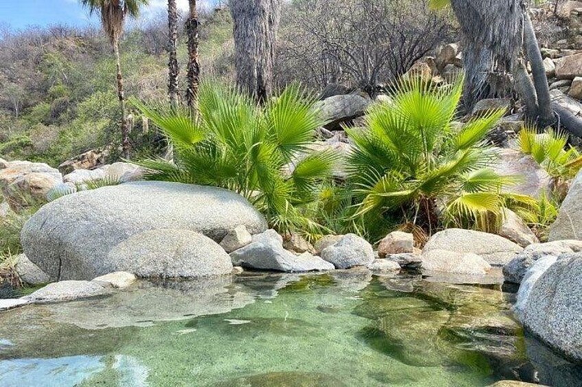 Masa de agua cristalina rodeada de rocas y palmeras. 2