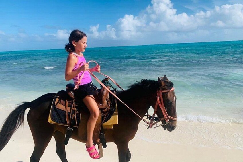 A person riding a horse on a beach with clear turquoise water. 2
