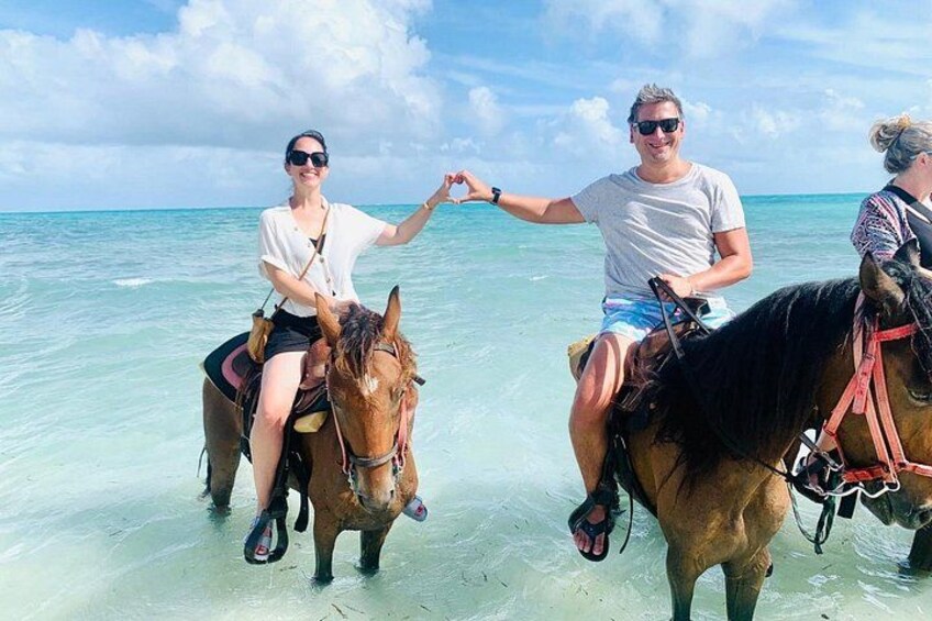 Two people riding horses on a beach with clear water and a blue sky. 5