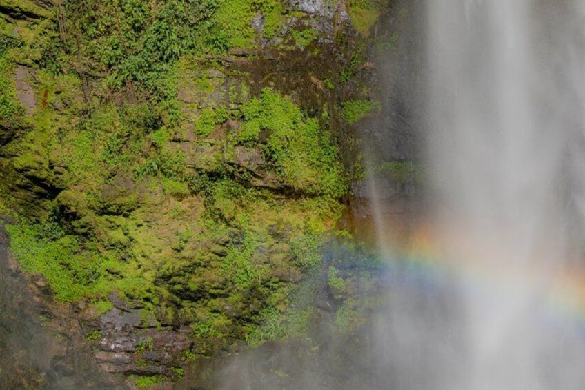 A waterfall cascading over a moss-covered cliff with a rainbow visible in the mist. 2