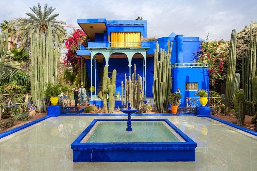 A blue building with a fountain, surrounded by cacti and palm trees. 3