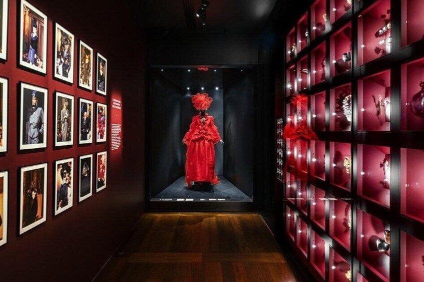 A hallway with a mannequin in a red dress, framed pictures on the walls, and red display cases. 2