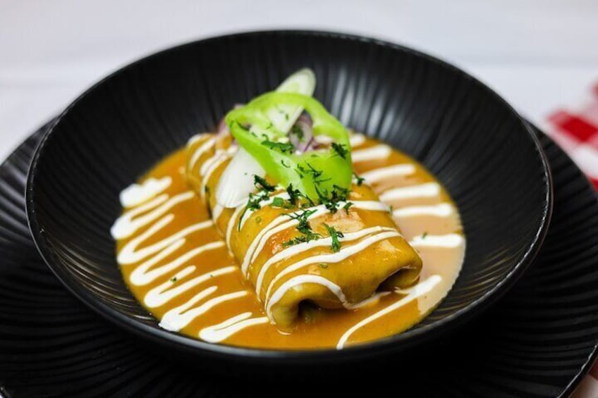 A rolled dish with sauce and garnish on a black plate. 4