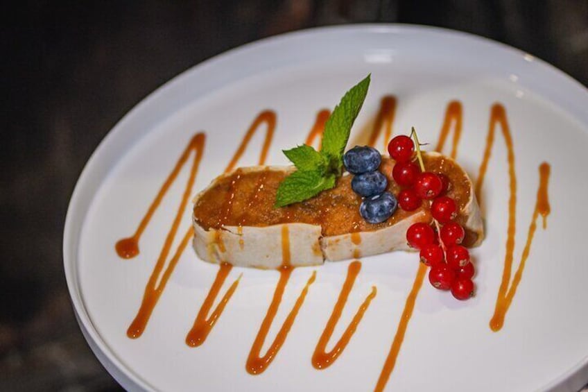 A dessert on a white plate with drizzled caramel sauce, blueberries, red currants, and a mint leaf. 3