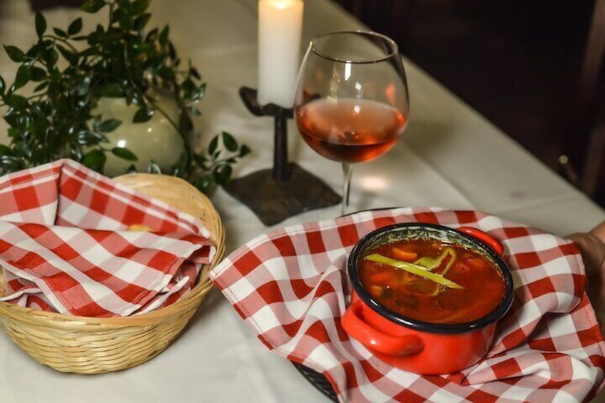 A bowl of soup on a red checkered napkin, a glass of red wine, and a candle on a table. 2