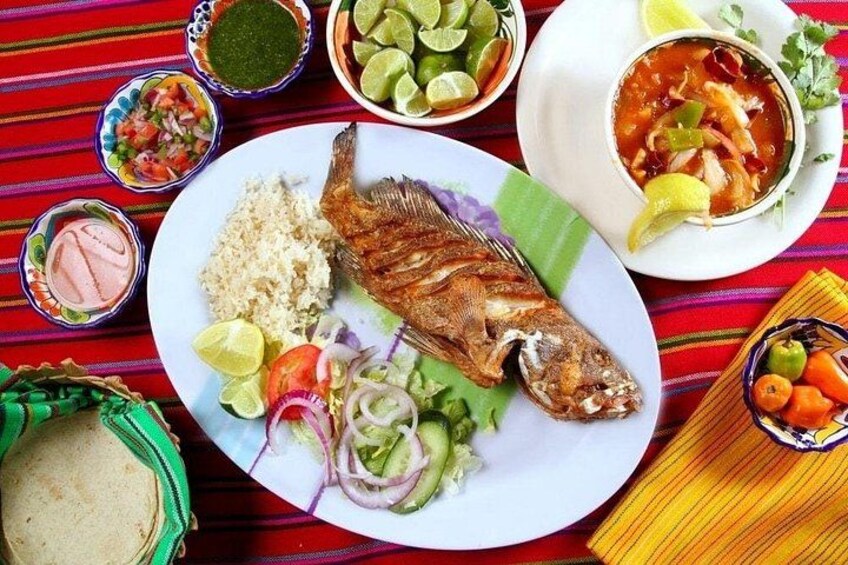 A plate with grilled fish, rice, and vegetables, accompanied by various condiments and a colorful tablecloth. 3