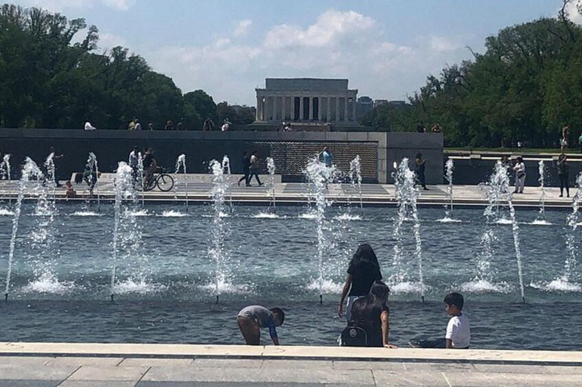 Une fontaine avec plusieurs jets d’eau, une personne penchée et un enfant debout près de l’eau. 2