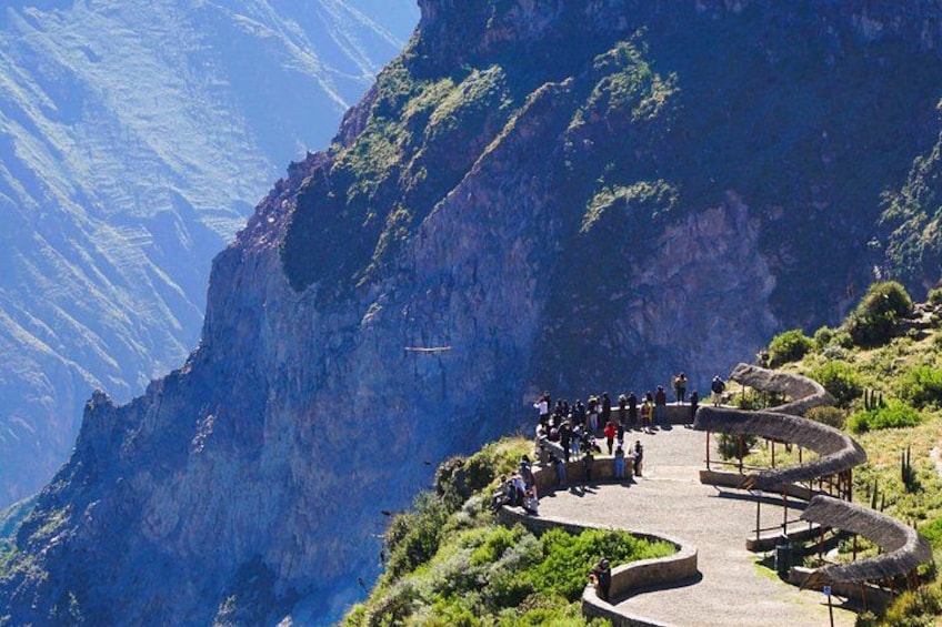 A winding mountain road with a group of people, a clear sky, and a steep cliffside. 1