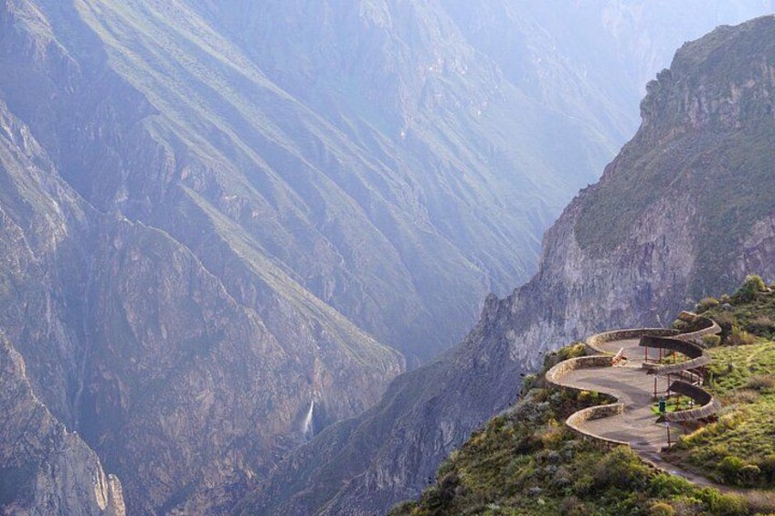 A winding mountain road with a guardrail, surrounded by steep cliffs and lush greenery. 4