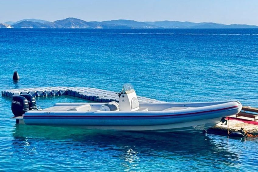 A small motorboat docked at a pier with clear blue water and distant mountains. 3