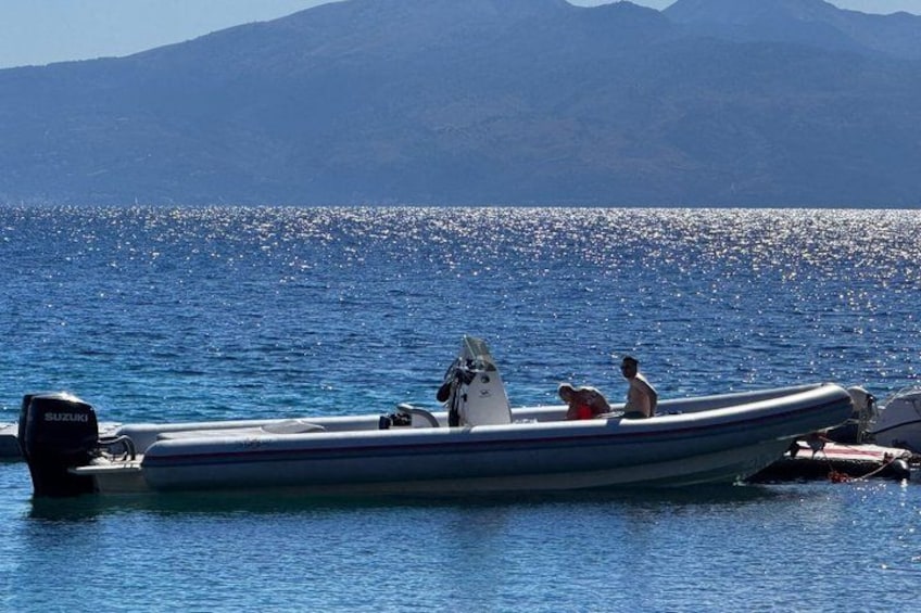A small inflatable boat with a Suzuki outboard motor, anchored near a body of water with a mountainous backdrop. 1