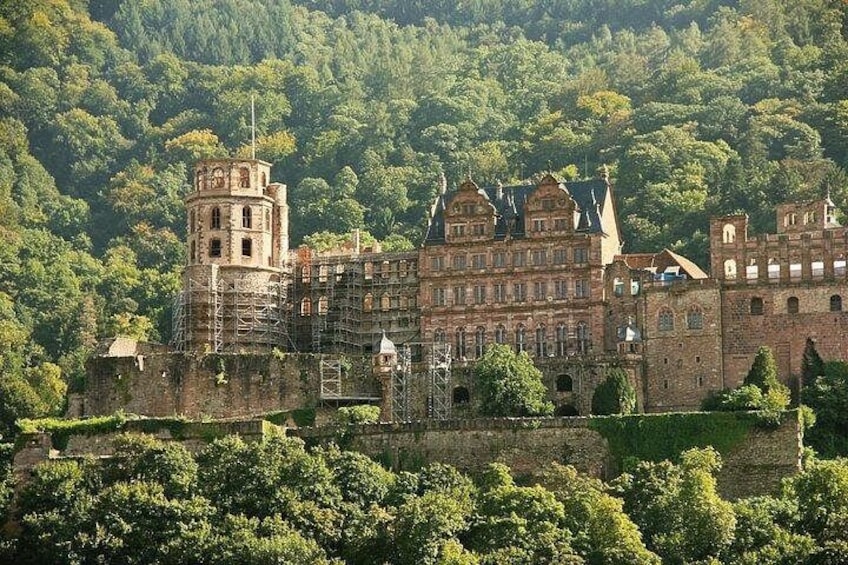 A historic castle with multiple towers, surrounded by lush greenery and a forested hill. 2