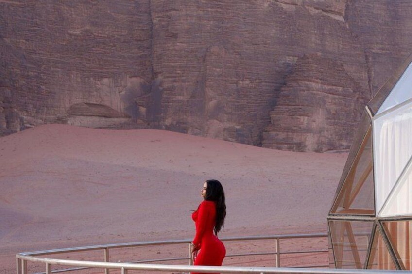 Una persona con un vestido rojo está de pie en un balcón que da a un paisaje desértico con formaciones rocosas. 2