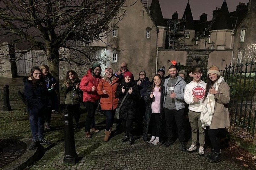A group of people standing on a cobblestone path in front of a historic building at night. 2