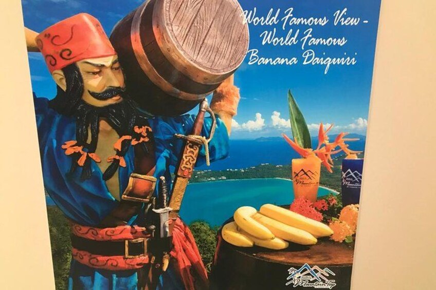 A person in traditional attire holding a wooden barrel, bananas, and a drink with a tropical background. 2