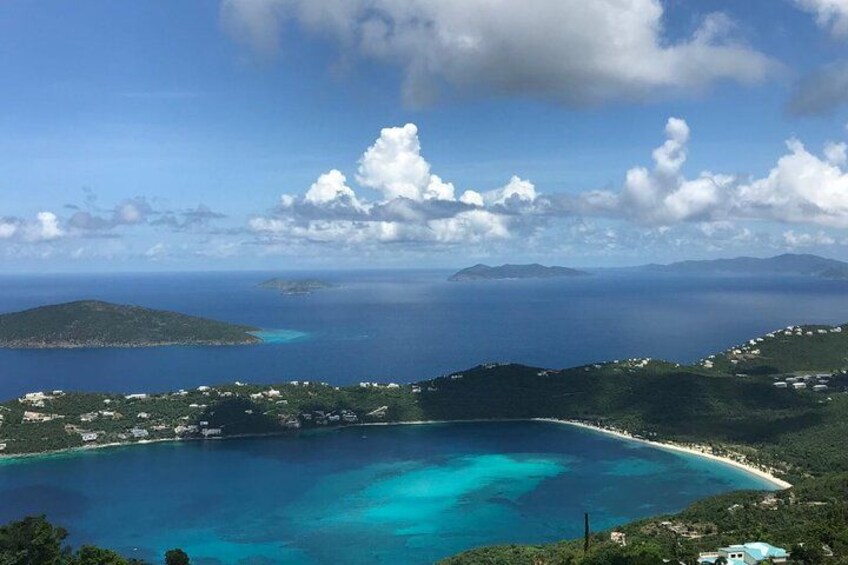 A coastal landscape with clear turquoise waters, a sandy beach, and lush green hills. 1