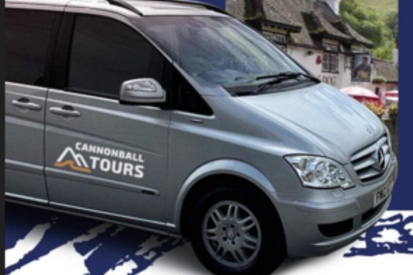 A silver van with 'Cannonball Tours' written on the side parked in front of a building with a thatched roof. 2