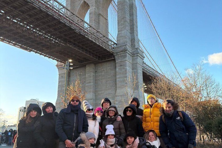 A group of people standing in front of a large stone bridge with multiple arches. 1