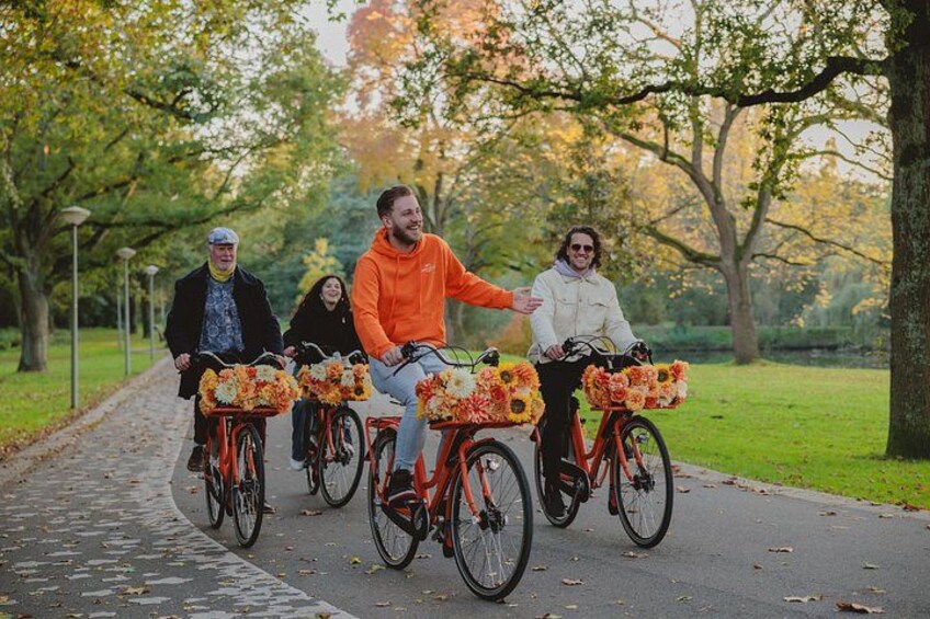 Four people riding bicycles on a paved path in a park with trees and grass. 2