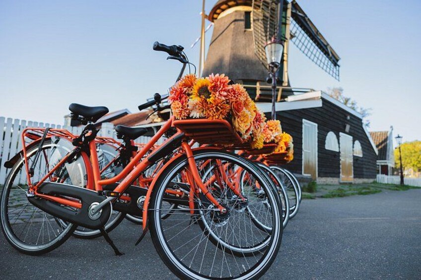 A red bicycle with a basket of flowers parked in front of a windmill. 5
