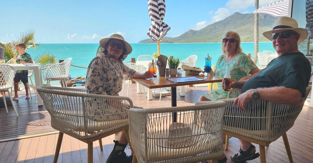 A tropical outdoor seating area with wicker chairs, a wooden table, and a view of the ocean. 5