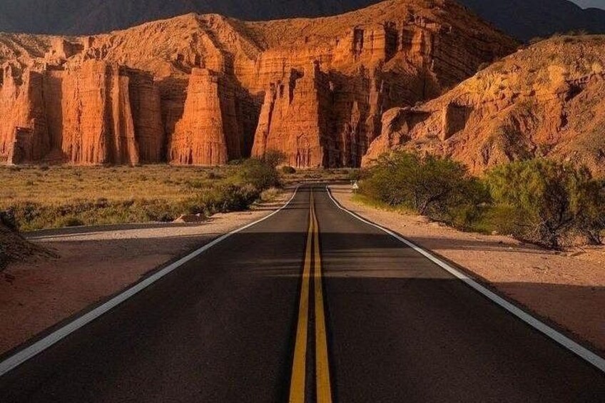 Una carretera con líneas amarillas dobles en un paisaje desértico con formaciones rocosas rojas. 2