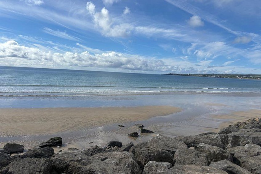 Una playa con rocas al frente, una orilla arenosa y un mar tranquilo bajo un cielo parcialmente nublado. 2