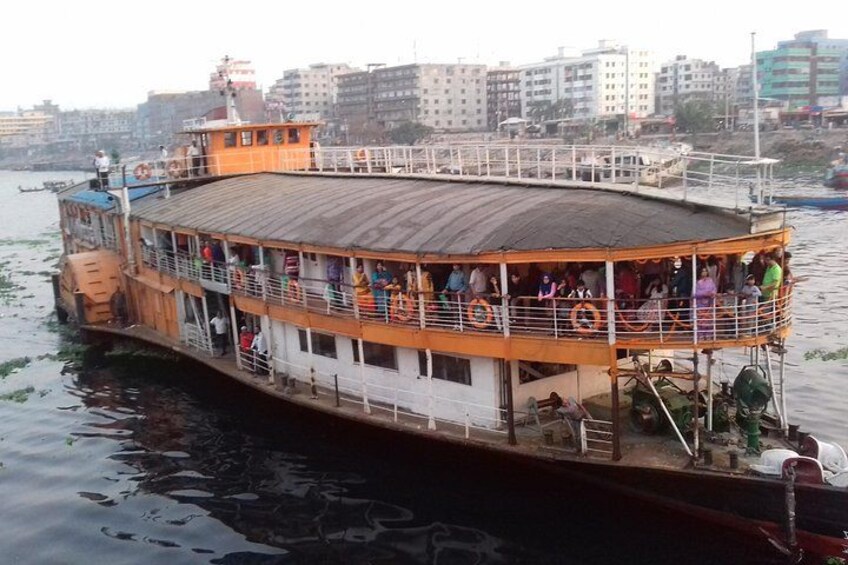 A riverboat with passengers on deck, surrounded by buildings and other boats. 2