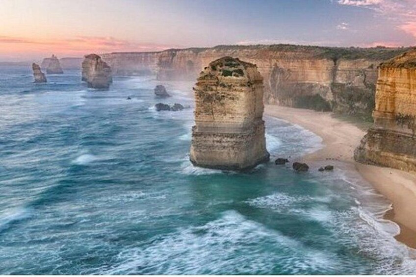 A coastal landscape with large rock formations and a sandy beach. 1