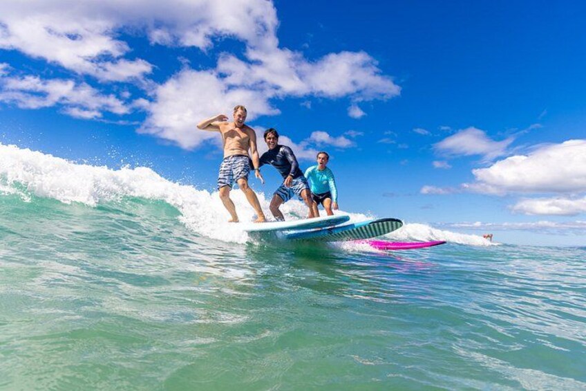 Three people surfing on a wave with a clear blue sky and ocean. 3