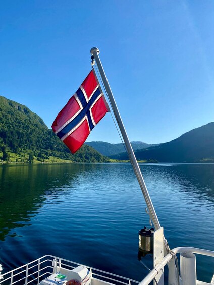 A flag on a boat, a lake, and mountains in the background. 1