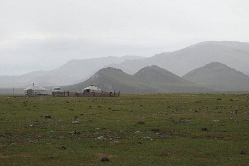 A grassy field with yurts and mountains in the background. 2