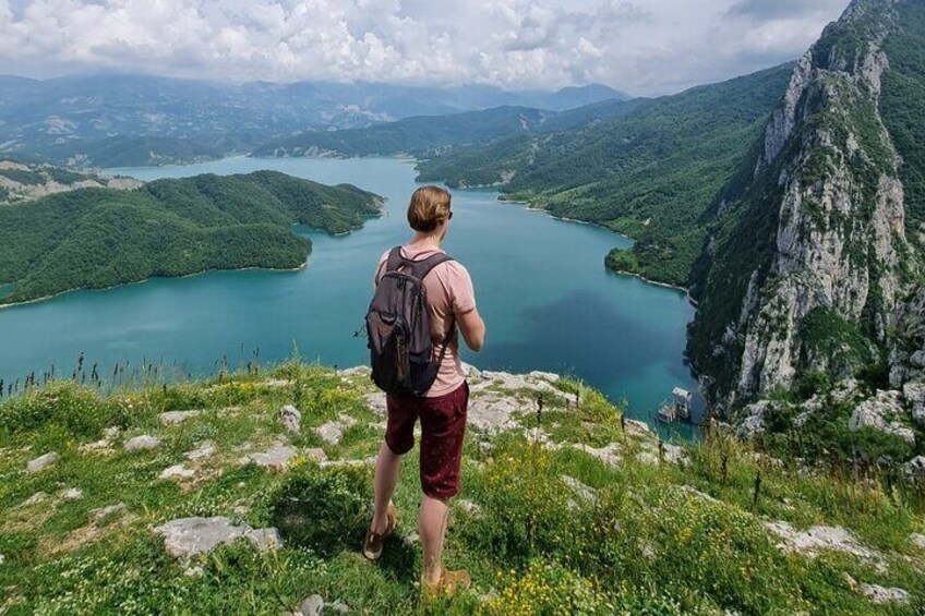 A person standing on a grassy hill overlooking a lake surrounded by mountains. 1