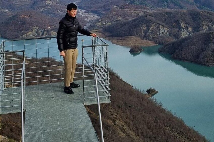 A person standing on a metal staircase overlooking a lake surrounded by hills. 5