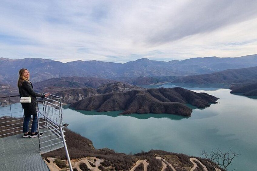 A person standing on a viewing platform overlooking a lake surrounded by mountains. 4