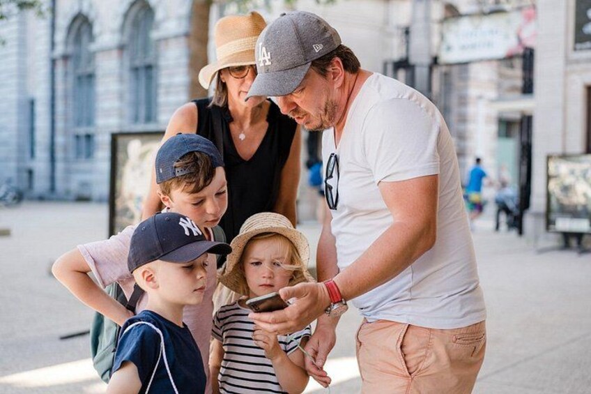 Un grupo de personas, entre ellos niños, de pie en una calle con edificios históricos al fondo. 5
